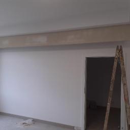 Usługi Ogólnobudowlane Robert Kolka - Pokój w trakcie wykańczania, ściany po szpachlowaniu, widoczna drabina oparta o framugę drzwi, sufit z elementem dekoracyjnym przed malowaniem.