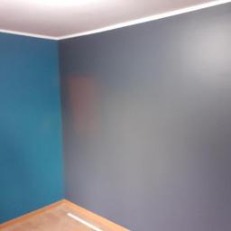 Usługi Ogólnobudowlane Robert Kolka - Pomieszczenie po malowaniu ścian na dwa kolory: turkusowy i szary, z widoczną drewnianą podłogą i białym paskiem na suficie.