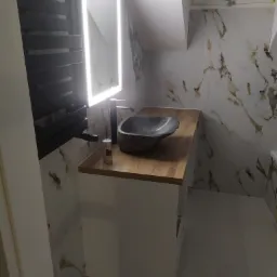 Nowoczesna łazienka na poddaszu z marmurowymi płytkami, drewnianym blatem, kamienną umywalką i podświetlanym lustrem LED.