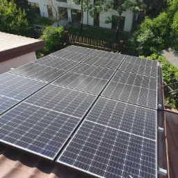 Panele słoneczne na dachu budynku w Warszawie, widok z góry, otoczenie zieleni i zabudowa miejska w tle.