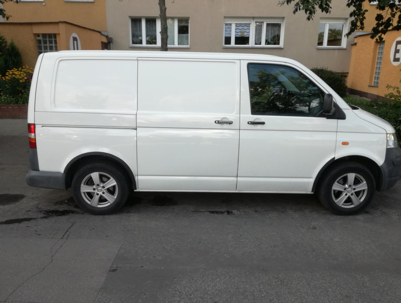 Biały samochód dostawczy typu furgon zaparkowany na ulicy, widok z boku na tle budynku mieszkalnego.