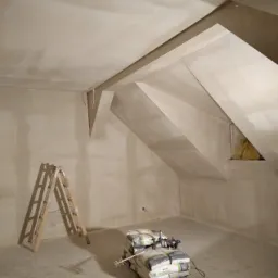 Poddasze w trakcie prac wykończeniowych: ściany i skosy świeżo pokryte gładzią, widoczne worki z zaprawą oraz drabina malarska w rogu pomieszczenia.