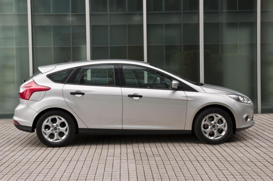 Srebrny hatchback zaparkowany na chodniku z szarej kostki, na tle nowoczesnego budynku z szklaną fasadą.