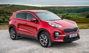 Czerwony samochód Kia Sportage na szutrowej drodze z zielonymi wzgórzami w tle, widok z przodu pod lekkim kątem.