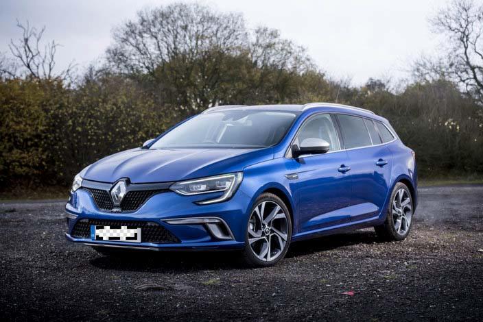 Niebieski samochód Renault Megane kombi z aluminiowymi felgami, zaparkowany na żwirowym podłożu z zamazaną tablicą rejestracyjną.
