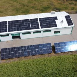 STROMER energia słoneczna i pompy ciepła - Widok z góry na budynek z panelami słonecznymi na dachu i na gruncie. Dwa samochody zaparkowane obok. Obok budynku widoczna zieleń.