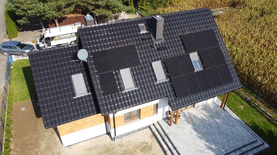 Instalacja paneli fotowoltaicznych na dachu domu jednorodzinnego w Bierdzanach. Widok z góry, panele wkomponowane w dach z dachówkami, obok okna dachowe.