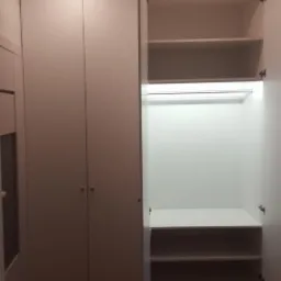 Biała szafa wnękowa z otwartymi drzwiami, ukazująca półki i oświetlenie LED, na tle parkietu ułożonego w jodełkę.