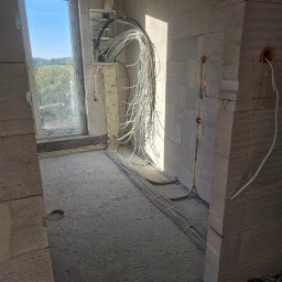 Hubert Żak - Surowy stan budynku w trakcie instalacji elektrycznej: kable w peszlach ułożone wzdłuż ściany i pod oknem, wiszące przewody z puszki elektrycznej zabezpieczone pianką montażową. Widoczne otwory...