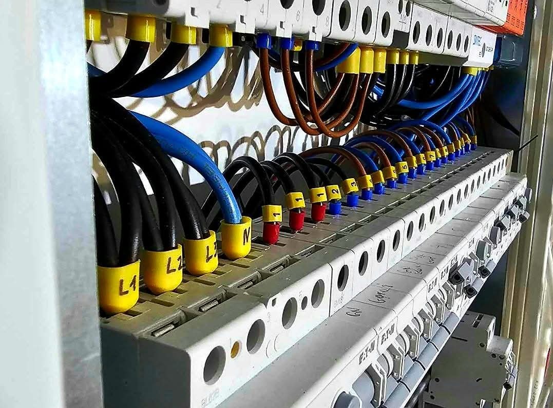 Szczegółowe ujęcie panelu elektrycznego z uporządkowanymi przewodami oznaczonymi kolorowymi tulejkami, widoczne kable czarne, niebieskie i brązowe, podłączone do listwy zaciskowej z opisami...