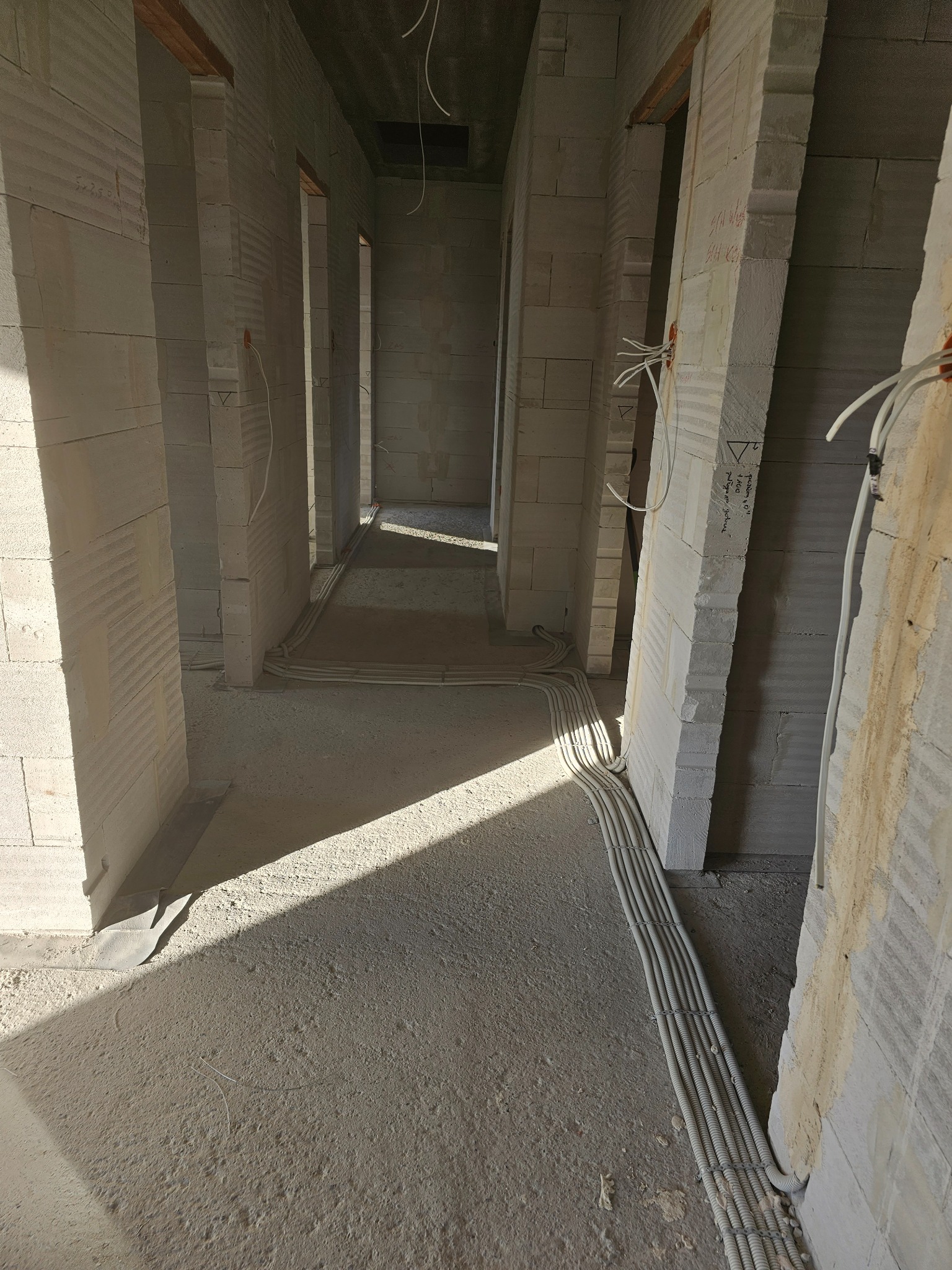 Wnętrze surowego budynku w trakcie instalacji elektrycznej: wiązka przewodów w peszlach ułożona wzdłuż ściany z betonu komórkowego, widoczne otwory drzwiowe i fragmenty instalacji w ścianach.