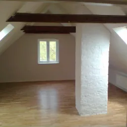 Puste poddasze po remoncie z drewnianą podłogą, białym słupem konstrukcyjnym i oknami dachowymi, widok na zewnątrz