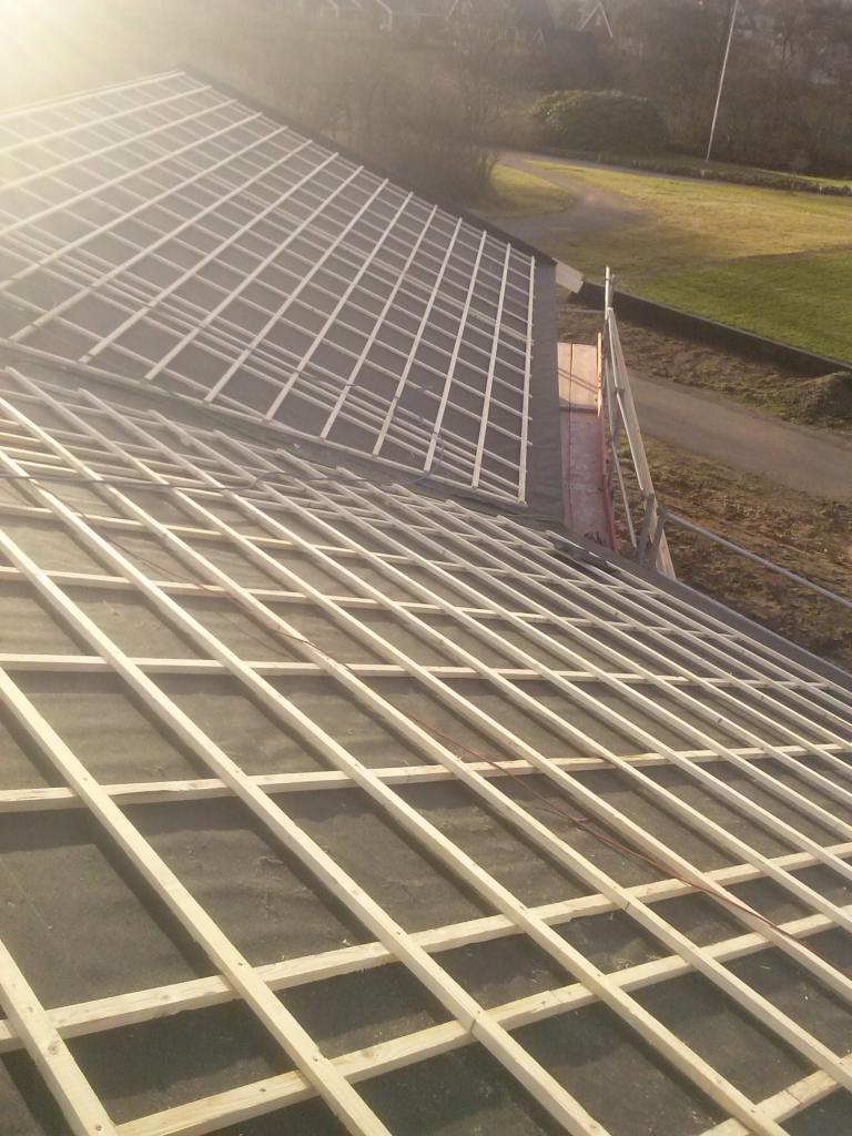 Konstrukcja drewniana dachu w trakcie budowy, widok z góry na szkielet z łat i kontrłat, w tle zielony krajobraz.