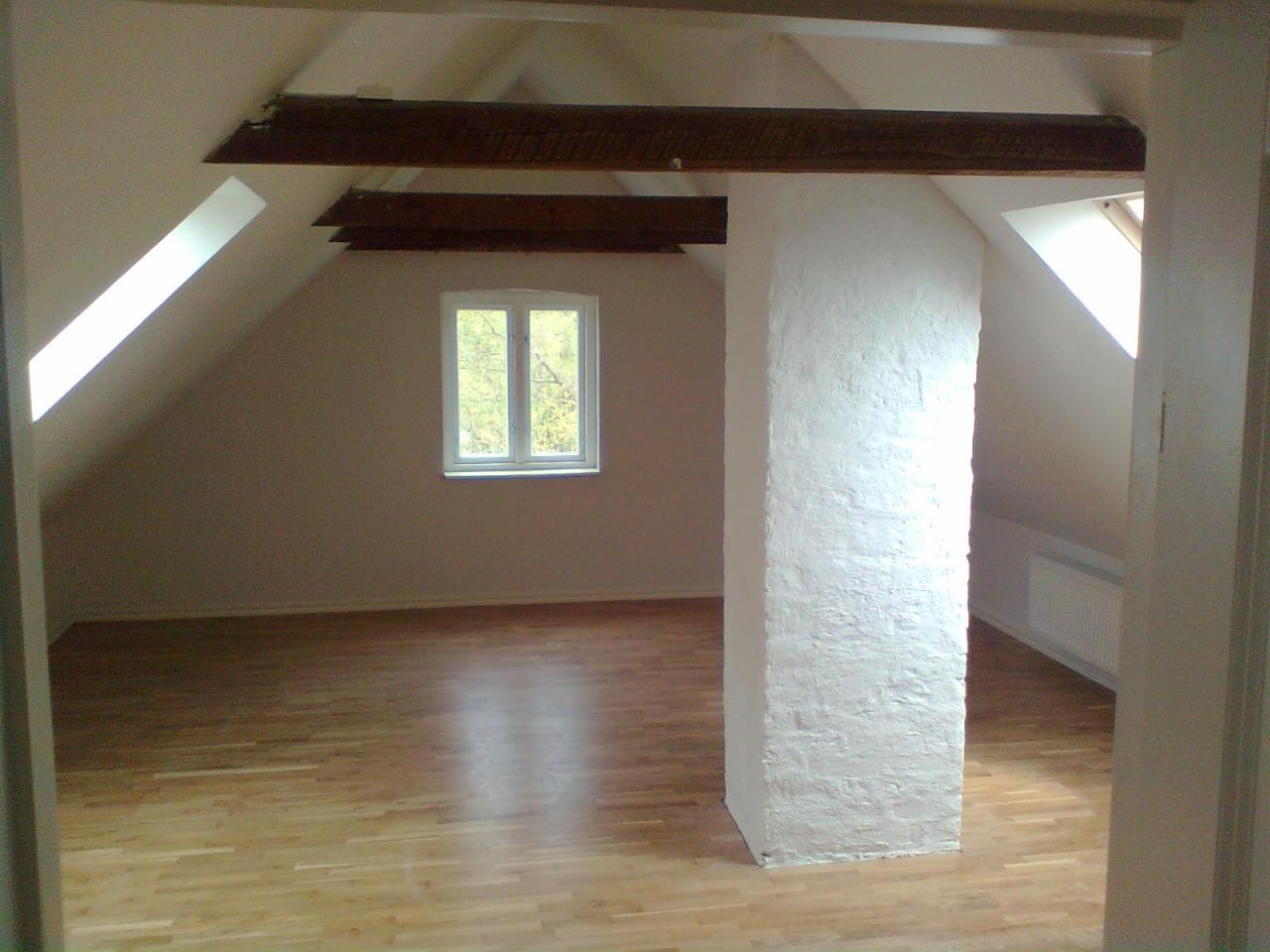 Puste poddasze po remoncie z drewnianą podłogą, białym słupem konstrukcyjnym i oknami dachowymi, widok na zewnątrz