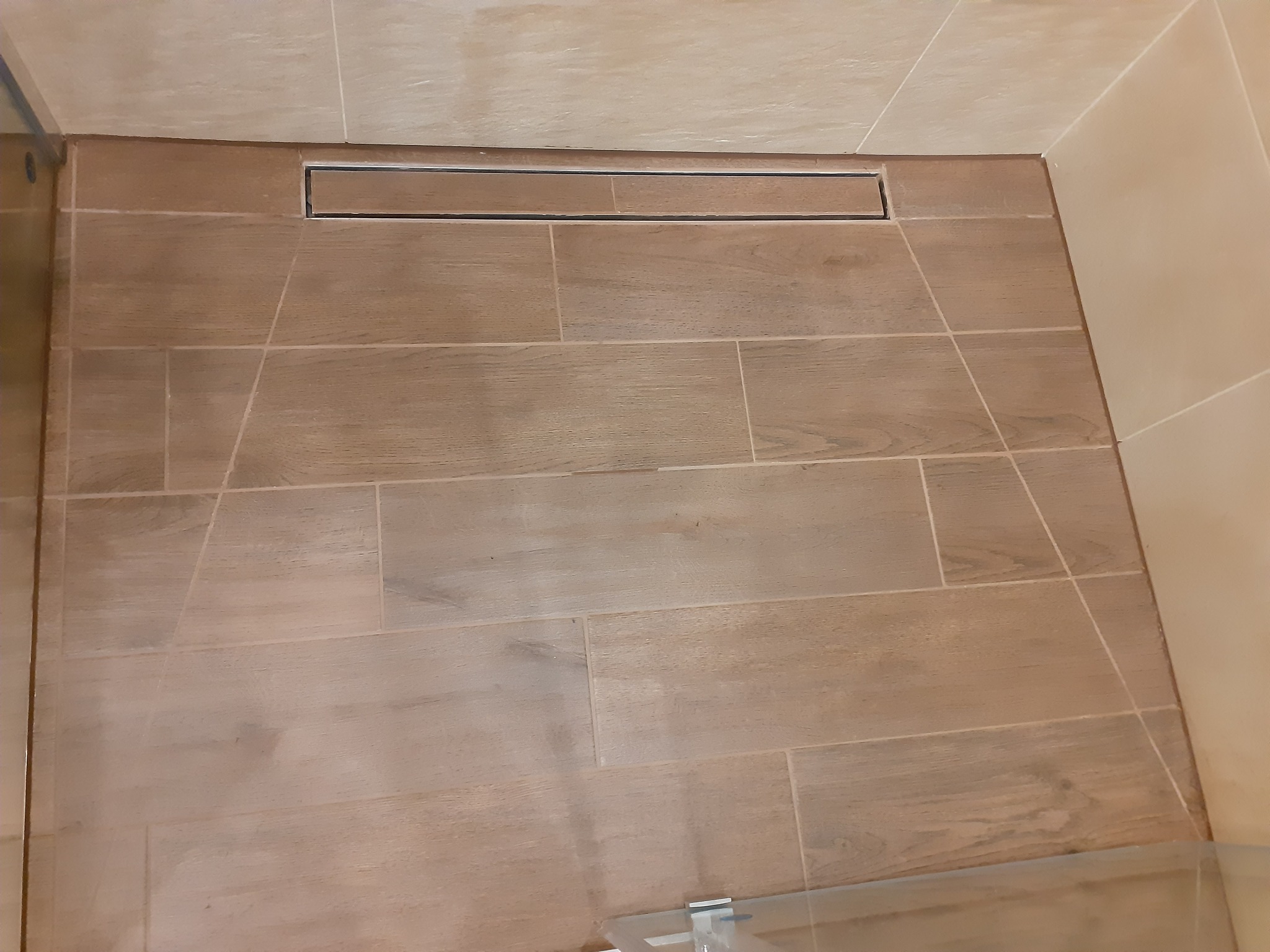 Wykończona kabina prysznicowa z odpływem liniowym w podłodze wyłożonej brązowymi płytkami imitującymi drewno.