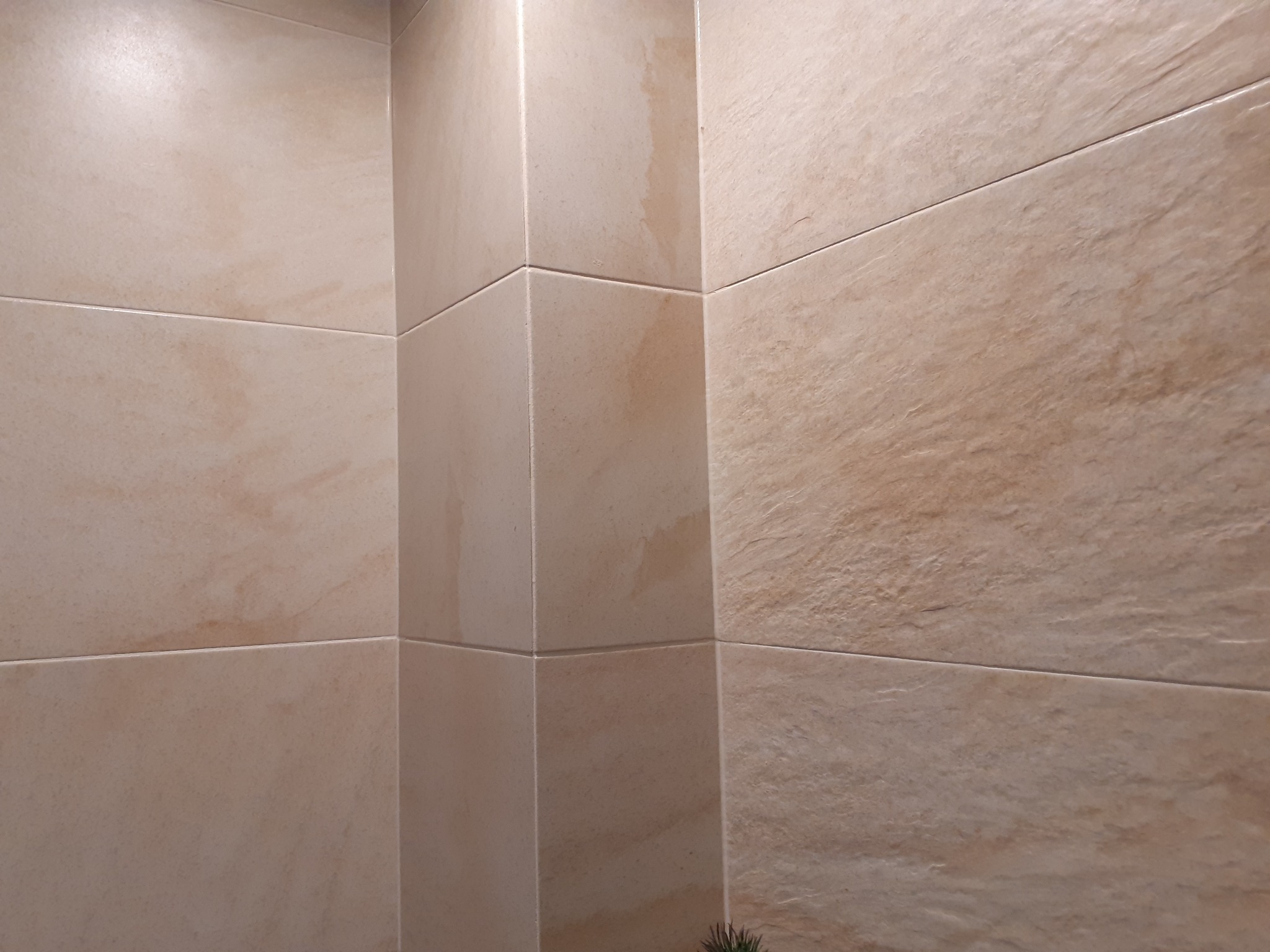 Beżowe płytki ceramiczne imitujące kamień, ułożone na ścianach w rogu pomieszczenia, z widocznymi fugami i delikatnym wzorem na powierzchni.