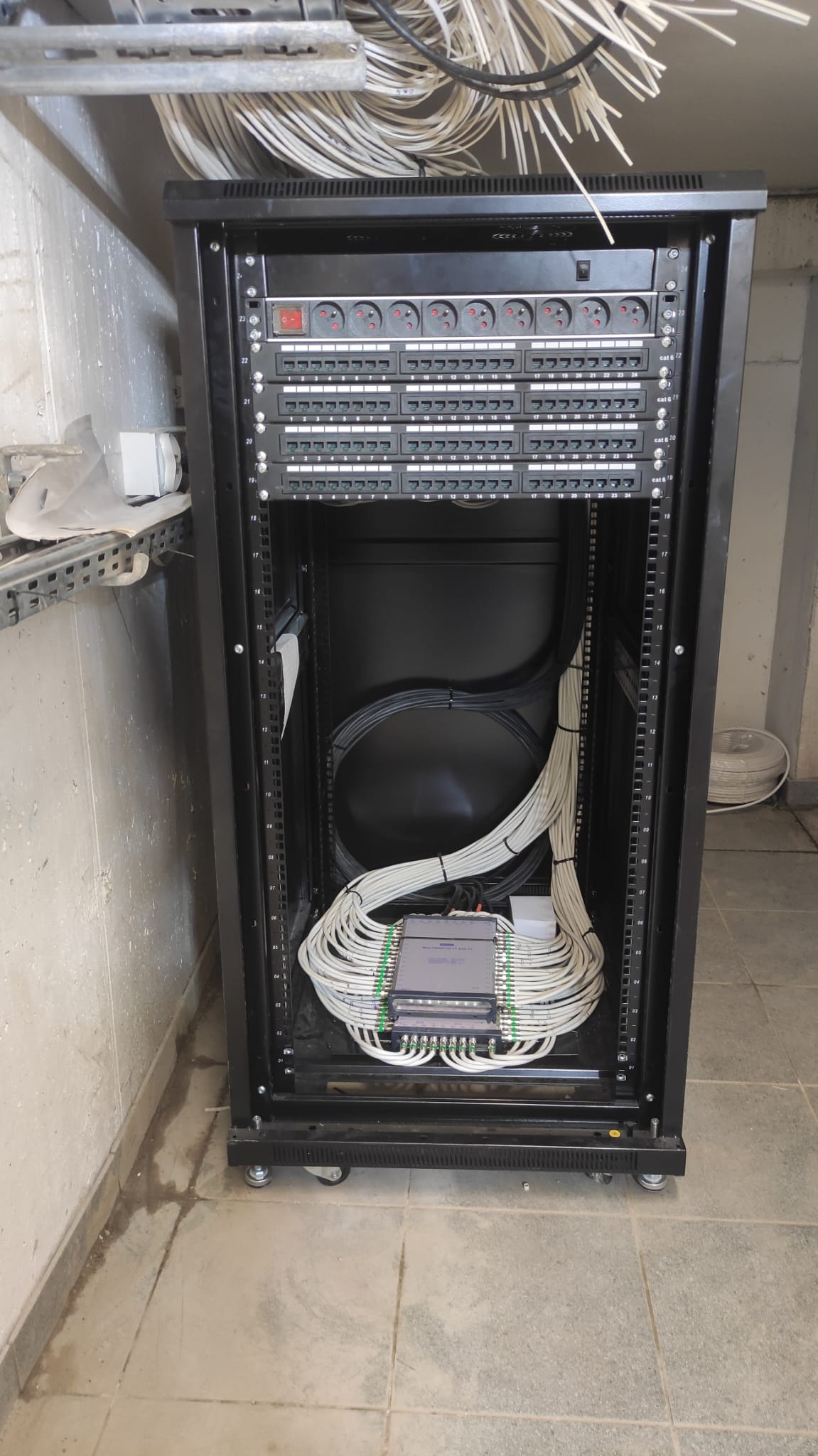 Szafa rack z patch panelem, listwami zasilającymi i uporządkowanymi kablami sieciowymi kategorii 6, widoczne kable prowadzone wewnątrz szafy.