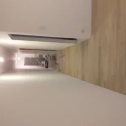 Długi korytarz w trakcie remontu: świeżo pomalowane ściany w jasnym odcieniu, ułożona drewniana podłoga i widoczny sprzęt malarski w głębi.