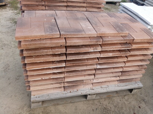 Stos brązowo-czerwonej kostki brukowej o geometrycznym wzorze, ułożonej na drewnianej palecie.