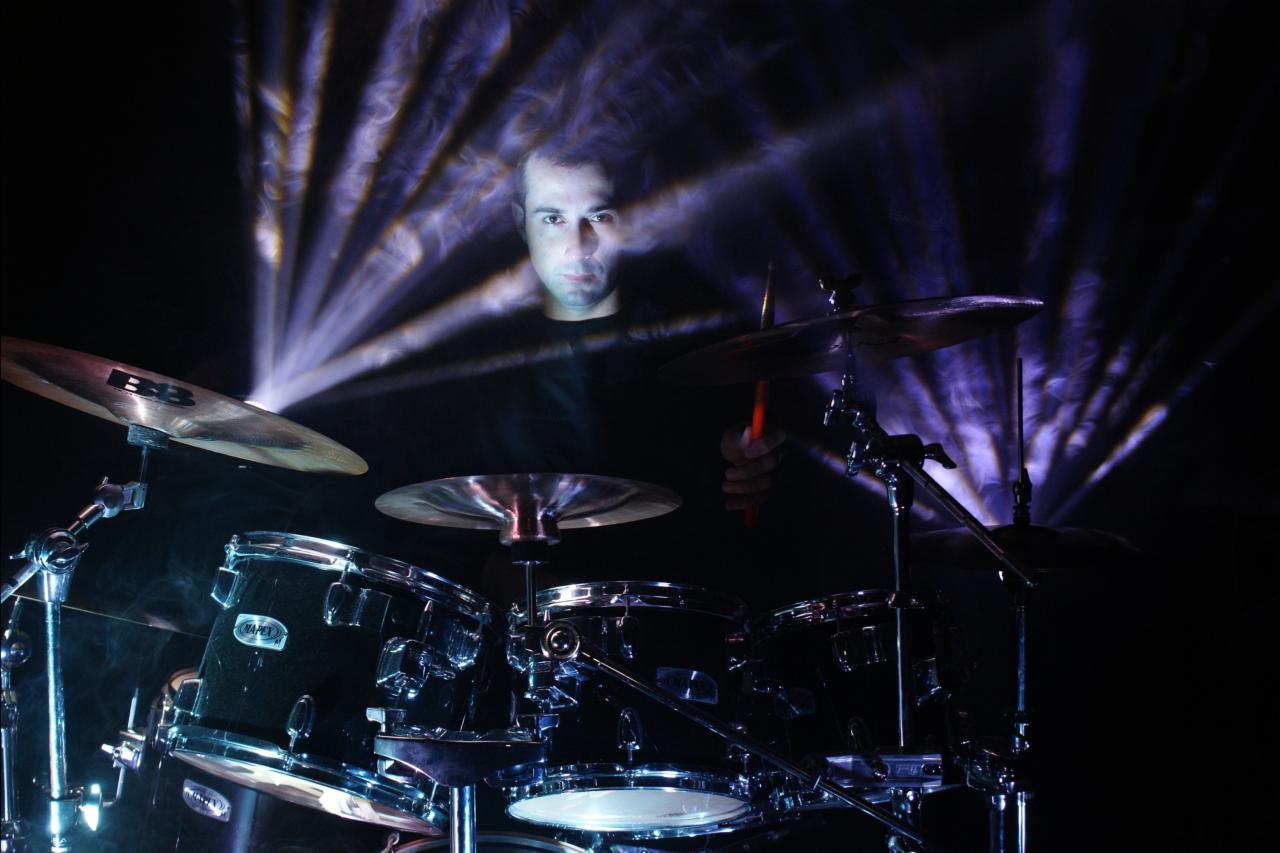 Perkusista z pałeczkami, oświetlony teatralnymi reflektorami podczas występu na scenie.