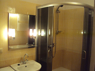 Jasna łazienka w Pobiedziskach po remoncie: kabina prysznicowa z chromowanymi profilami, umywalka z baterią i lustro z oświetleniem. Widoczne beżowe płytki na ścianach.