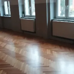 Ułożony parkiet w jodełkę w pustym pokoju z grzejnikami pod oknami, widok z góry.