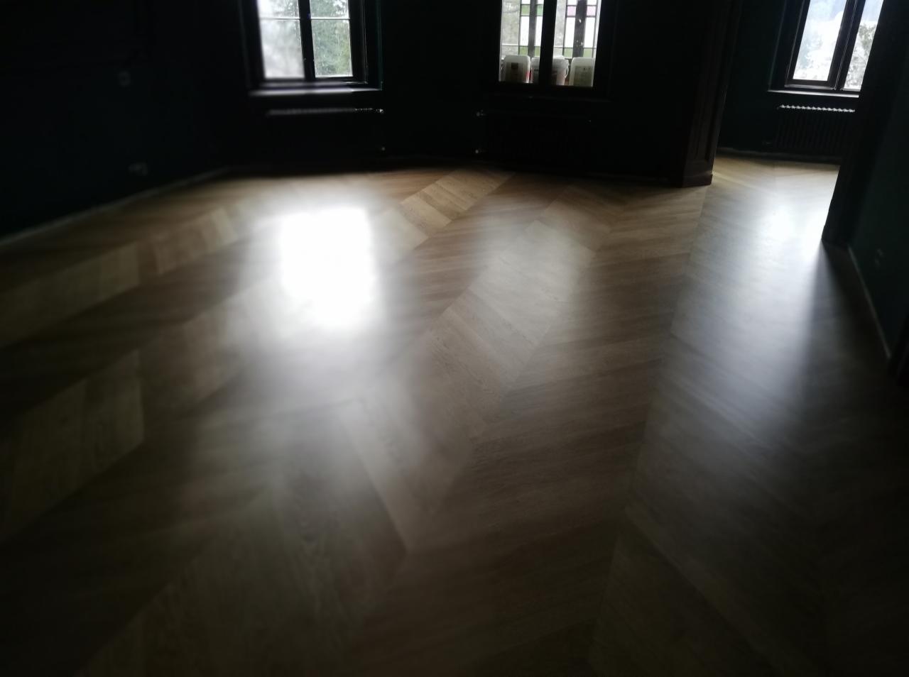 Nowo ułożony parkiet w jodełkę francuską w słabo oświetlonym pokoju z ciemnymi ścianami i oknami.