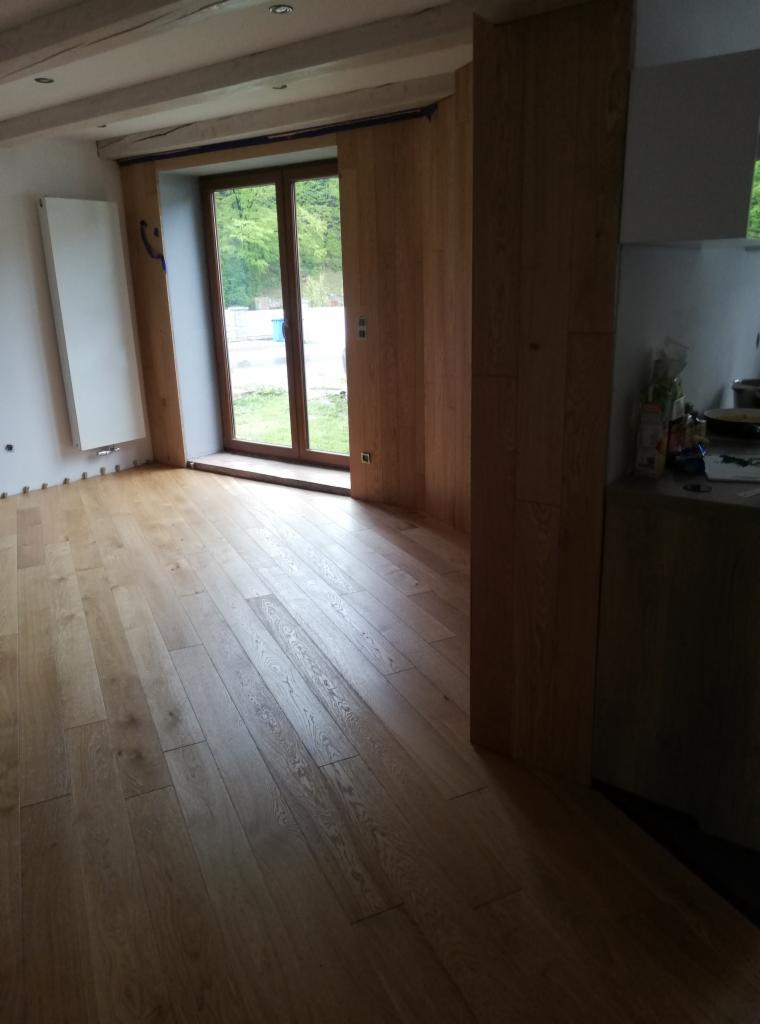 Jasna, świeżo położona podłoga z desek parkietowych w nowym wnętrzu z oknem i grzejnikiem, widoczne listwy przypodłogowe w trakcie montażu.