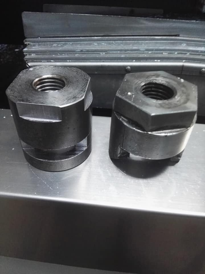 Dwa metalowe elementy z gwintem wewnętrznym i sześciokątną podstawą, leżące na metalowej powierzchni, widoczne ślady obróbki.