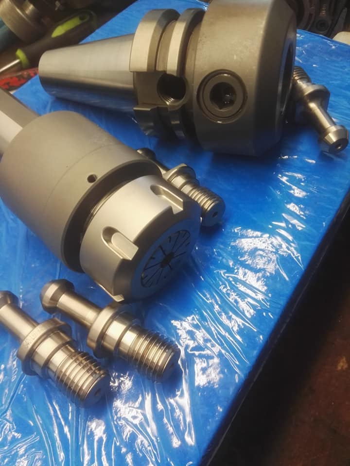 Metalowe uchwyty narzędziowe i trzpienie mocujące na niebieskim podłożu, widoczne ślady obróbki skrawaniem.