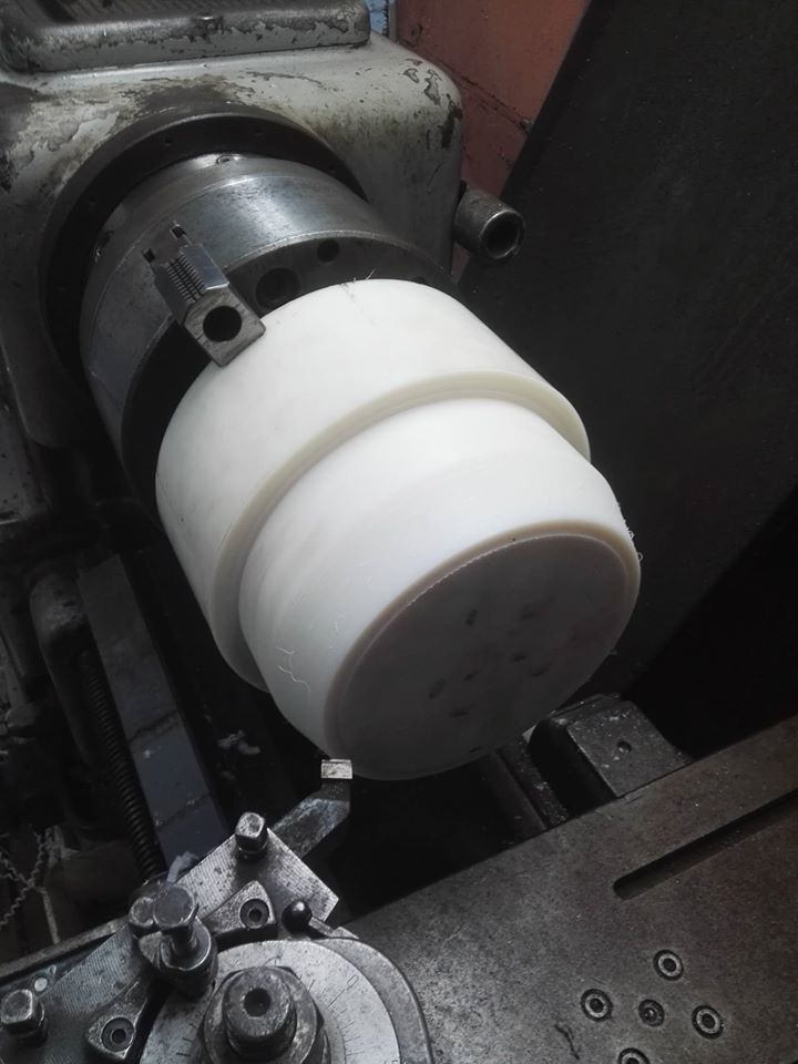 Biały, obracający się walec z tworzywa sztucznego zamocowany w uchwycie tokarki podczas obróbki skrawaniem.