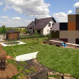 Widok z góry na świeżo założony trawnik z rolki, z białym żwirowym chodnikiem, młodymi drzewkami, altaną i nowym domem w tle.