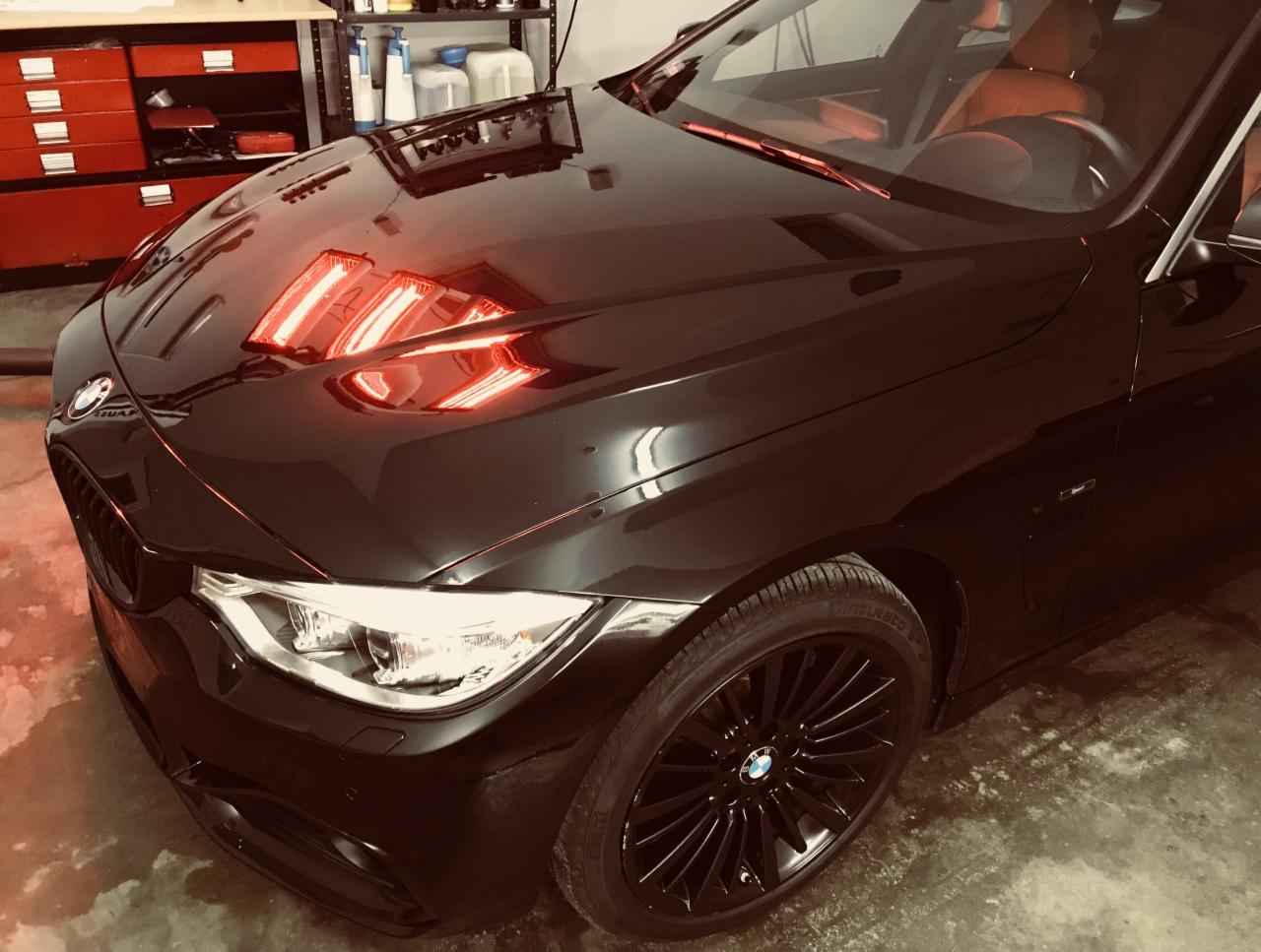 Błyszczący czarny samochód marki BMW poddawany suszeniu lakieru za pomocą lamp na podczerwień, widoczne odbicia w lakierze.