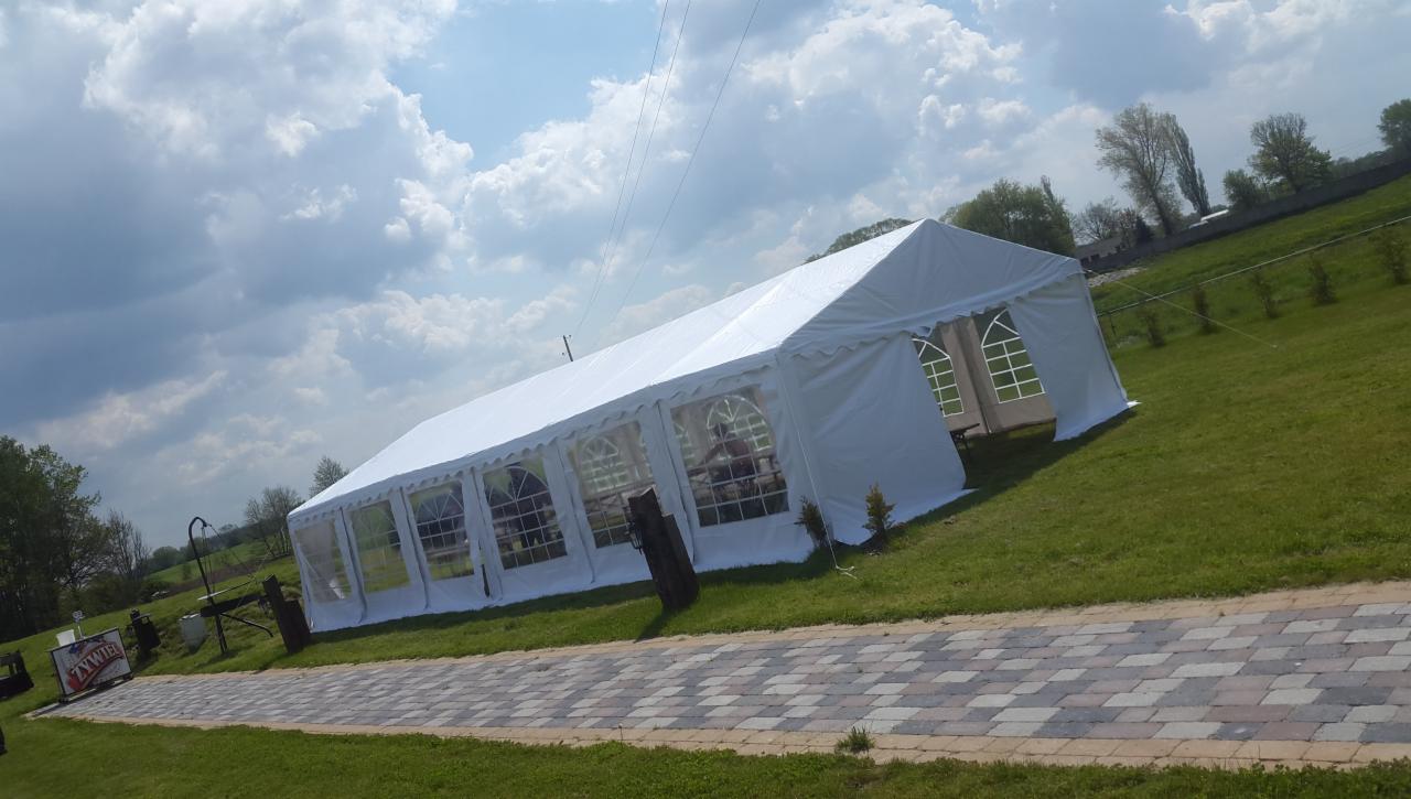 Biały namiot imprezowy z oknami na trawniku w słoneczny dzień, widok z boku na ścieżkę z kostki brukowej i logo Żywiec w tle.