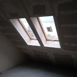 Poddasze w trakcie wykańczania z trzema oknami dachowymi, ściany i sufit pokryte płytami karton-gips z widocznymi łączeniami wymagającymi szpachlowania.