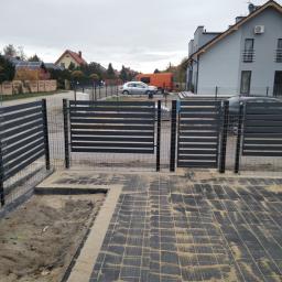 Przem-Bud - Nowoczesne, poziome przęsła ogrodzeniowe z metalu w kolorze antracytowym, zamontowane na posesji z kostką brukową; widoczny fragment terenu przygotowanego pod nasadzenia.