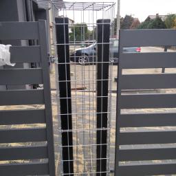 Przem-Bud - Nowoczesna, grafitowa brama wjazdowa z metalowymi słupkami wypełnionymi siatką gabionową, widok z zewnątrz posesji.