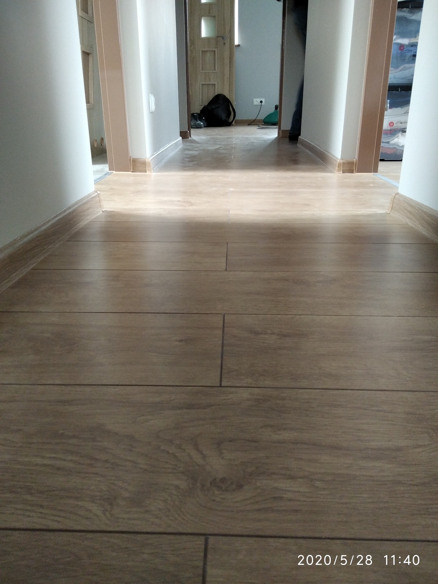 Ułożone panele podłogowe w korytarzu, widok wzdłuż pomieszczenia, z widocznymi listwami przypodłogowymi i otwartymi drzwiami w tle.