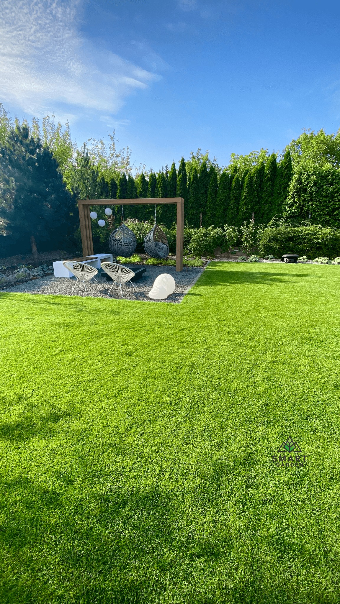 Zadbany trawnik w Warszawie z drewnianą konstrukcją z wiszącymi fotelami i kulistymi lampami, otoczony zielenią i iglakami.