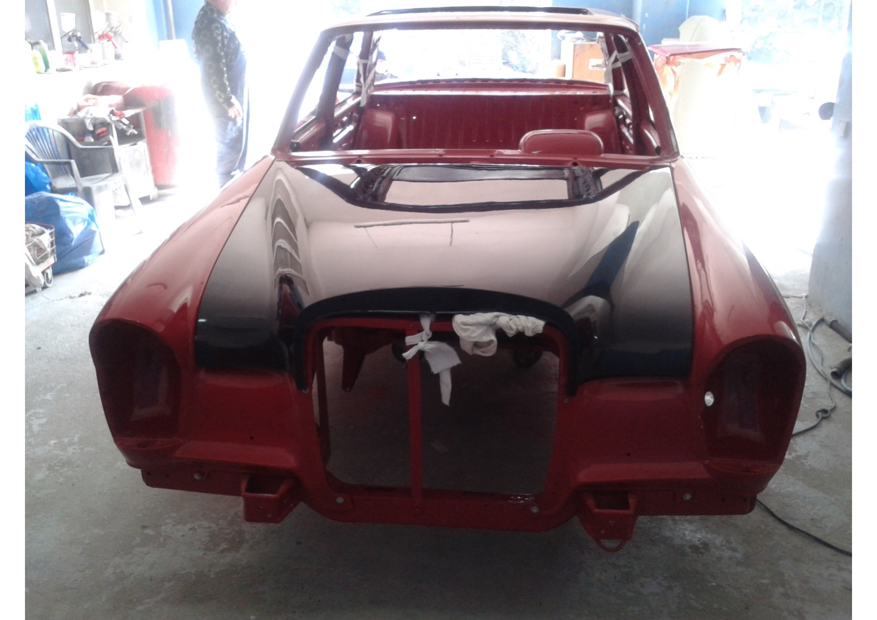 Czerwone nadwozie samochodu bez przednich świateł i atrapy chłodnicy, z czarnym, błyszczącym lakierem na masce, w trakcie prac blacharsko-lakierniczych.