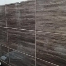 Ukończona ściana łazienki z brązowo-białymi płytkami imitującymi marmur, z widocznym fragmentem uchwytu na papier toaletowy w lewym dolnym rogu.