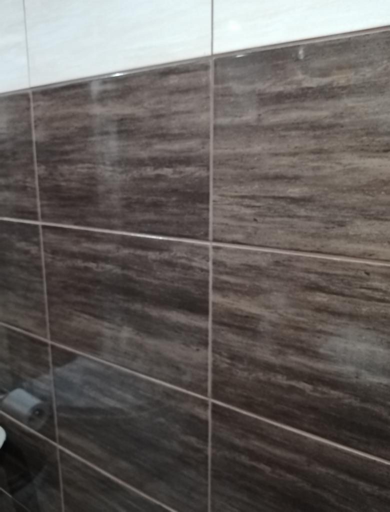 Ukończona ściana łazienki z brązowo-białymi płytkami imitującymi marmur, z widocznym fragmentem uchwytu na papier toaletowy w lewym dolnym rogu.