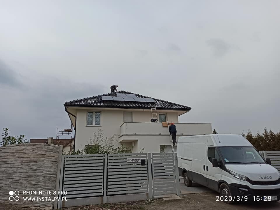 Montaż paneli słonecznych na dachu domu jednorodzinnego przez dwóch instalatorów, z użyciem drabiny i białego samochodu dostawczego Iveco na podjeździe.