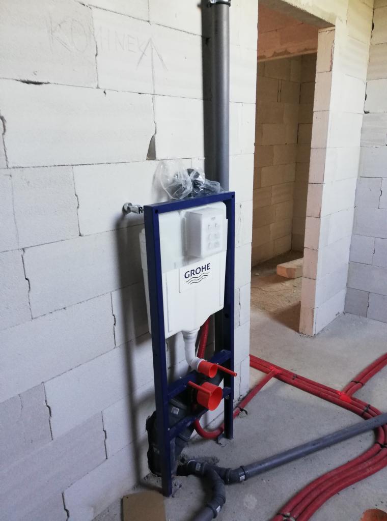Stelaż podtynkowy WC marki Grohe zamontowany przy ścianie z białego betonu komórkowego, widoczne rury doprowadzające wodę i odpływ kanalizacyjny w surowym stanie.