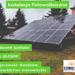 Naziemna instalacja fotowoltaiczna o mocy 10.01 kW, producent JustSolar, zlokalizowana w Kazanowie, województwo mazowieckie, widoczna na tle zielonej trawy i drzew iglastych.