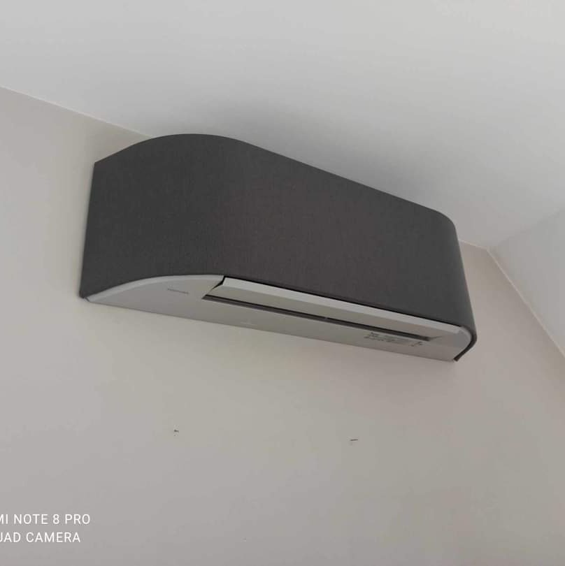 Szary klimatyzator ścienny zamontowany w rogu pomieszczenia, widok z dołu.