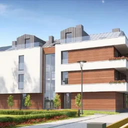 Nowoczesny budynek apartamentowy z drewnianą elewacją i białymi balkonami z kwiatami, otoczony zielenią i niskimi krzewami, oświetlony popołudniowym słońcem.