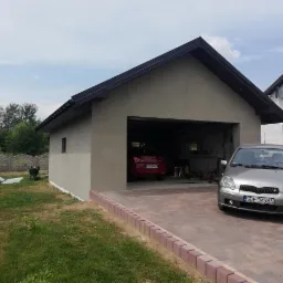 Nowo otynkowany garaż z dwoma samochodami, jeden czerwony w środku, drugi srebrny na podjeździe z kostki.