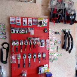 Ekspozycja akcesoriów rowerowych na czerwonej perforowanej ścianie: narzędzia, oświetlenie, błotniki, foteliki dziecięce w folii, części zamienne.