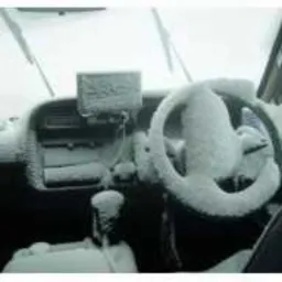 Wnętrze samochodu pokryte śniegiem, widoczne deska rozdzielcza, kierownica i przednia szyba z wycieraczkami, wszystko oszronione.